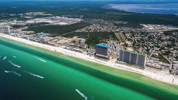 An aerial view of a coastal city with a prominent hotel featuring a modern design, located near a beach with clear turquoise waters. - Sunrise Resort by BBG (Panama City Beach)