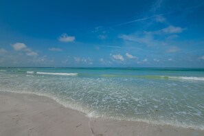 A beach with clear turquoise water, gentle waves, and a sandy shore. - New Listing Sunset Tropical Beach Bungallow (Treasure Island)