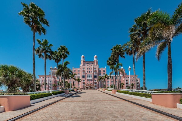 A large, pink, multi-story hotel with a central entrance and palm trees lining the pathway. - New Listing Sunset Tropical Beach Bungallow (Treasure Island)