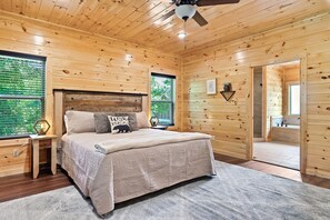 Een houten slaapkamer met een bed, nachtkastjes, een plafondventilator en uitzicht op het omliggende landschap.