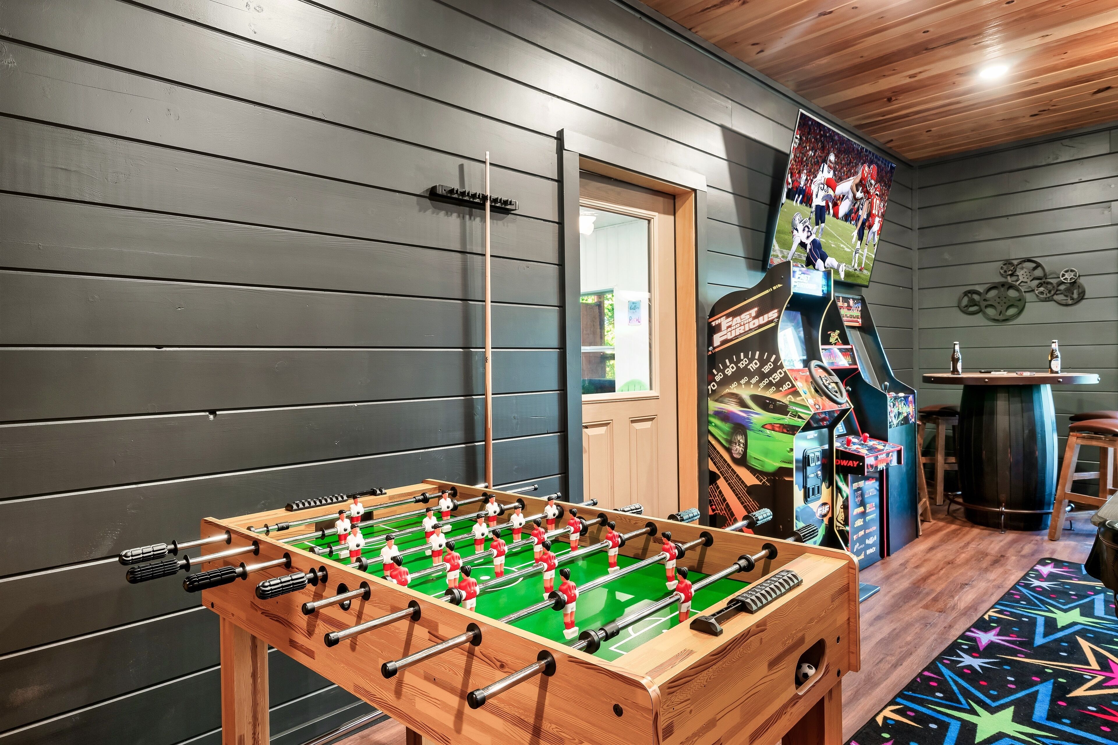Una habitación con mesa de fútbol, zona de bar con juegos arcade y una alfombra con estampado de estrellas.