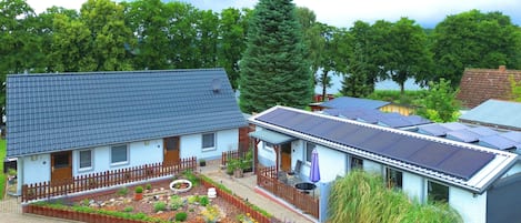 Ett hus med ett solpanelbeklätt tak, en inhägnad trädgård och ett stort träd i bakgrunden.