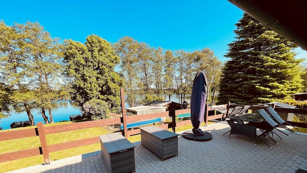 Un patio con mobiliario exterior, piscina y vistas a árboles y un lago.