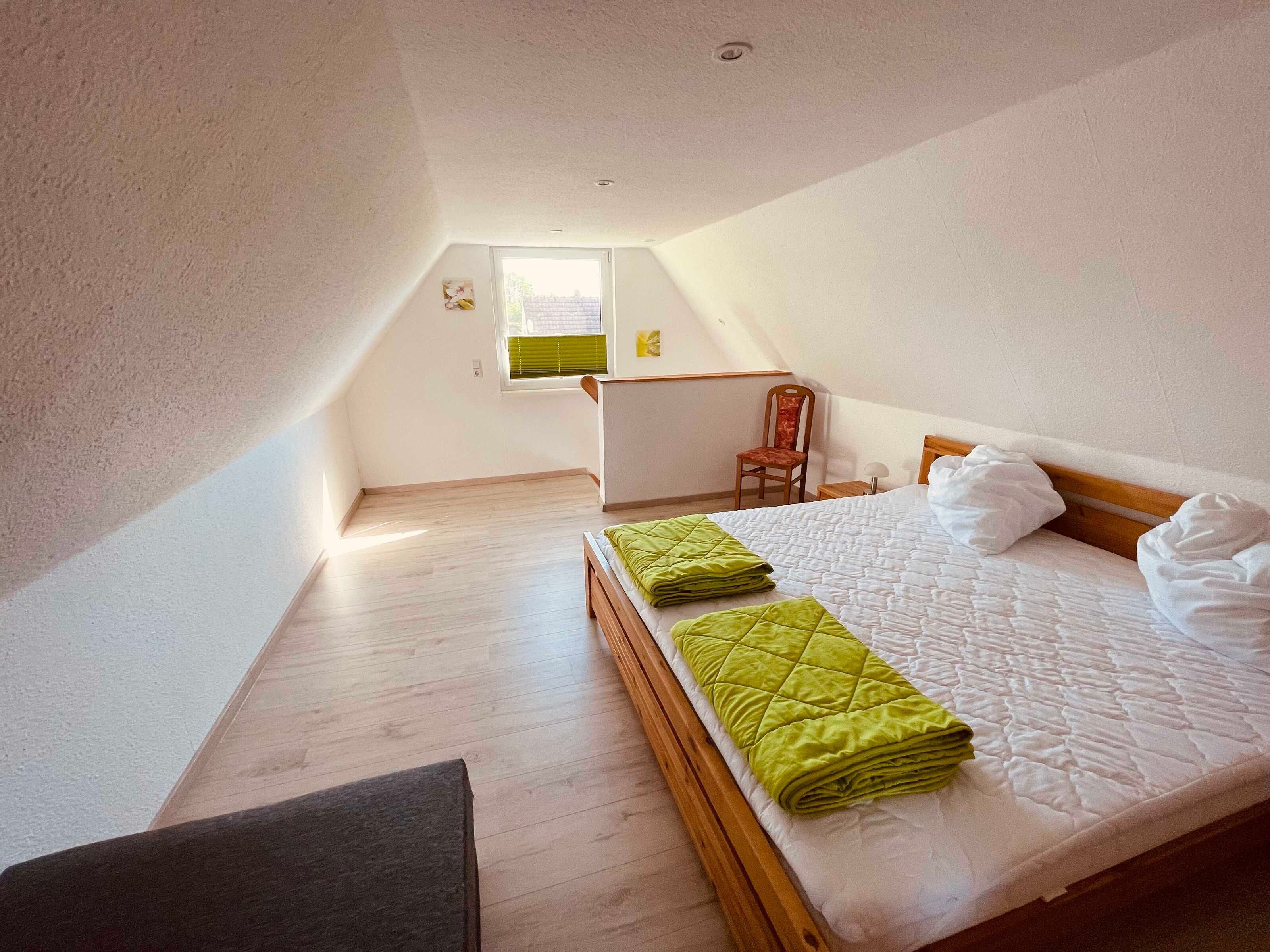 A bedroom with a bed, a chair, a desk, and a window.
