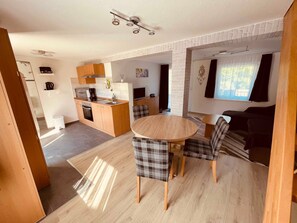 Una cocina moderna con una isla central, un comedor con sillas a cuadros y una sala de estar con sofá y televisor.