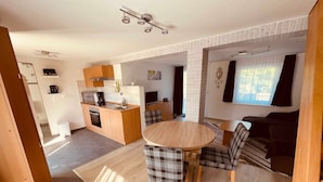 Una cocina moderna con una isla central, un comedor con sillas a cuadros y una sala de estar con sofá y televisor.