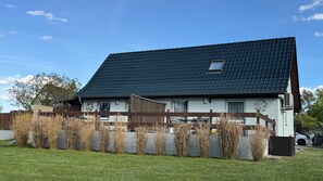 A two-story house with a dark tiled roof, a small window, and a fenced yard with tall grass.