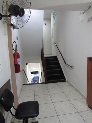 A stairwell with a fire extinguisher, a fan, and a chair. - Hotel Pauliceia (São Paulo)