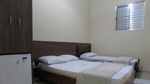 Un dormitorio con dos camas individuales, un armario de madera y un refrigerador pequeño.