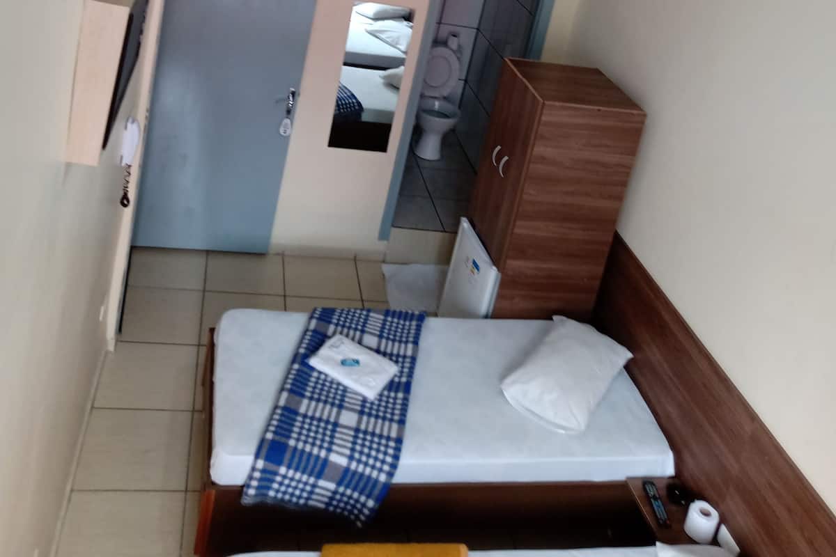 Pieni hotellihuone, jossa on sänky, pieni puinen kaappi, kattotuuletin ja kylpyhuone, joka näkyy avoimesta ovesta.