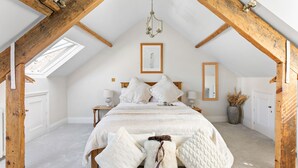 A bedroom with a sloped ceiling, exposed wooden beams, a bed with white bedding, a chandelier, and a framed picture on the wall. - 1 Quayside, Heart Of Appledore - Free WiFi - Wood Burner - Coffee Machine (Appledore)