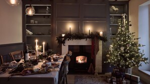 A warmly lit dining area with a fireplace, a Christmas tree, and a table set for a meal. - 1 Quayside, Heart Of Appledore - Free WiFi - Wood Burner - Coffee Machine (Appledore)