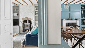 A cozy living room with a fireplace, a dining area with a table set for two, and a kitchen area with blue cabinets. - 1 Quayside, Heart Of Appledore - Free WiFi - Wood Burner - Coffee Machine (Appledore)