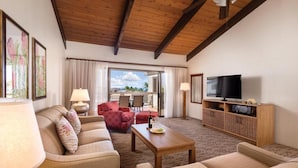 A spacious living room with a wooden ceiling, a television, a sofa set, and a dining area with a table and chairs.