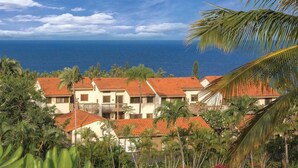 A resort with multiple buildings, red-tiled roofs, and a view of the ocean.