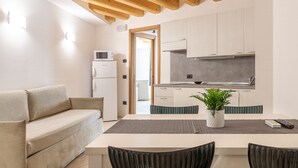 A modern kitchen with white cabinets, a microwave, and a built-in oven. There is a dining table with chairs and a potted plant.