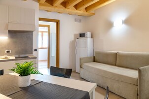 A modern kitchen with a dining table, a sofa, and a refrigerator.