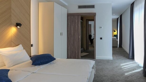 A hotel room with a large bed, a wardrobe, and a bathroom visible through an open door. - Hotel Mir (Cajetina)