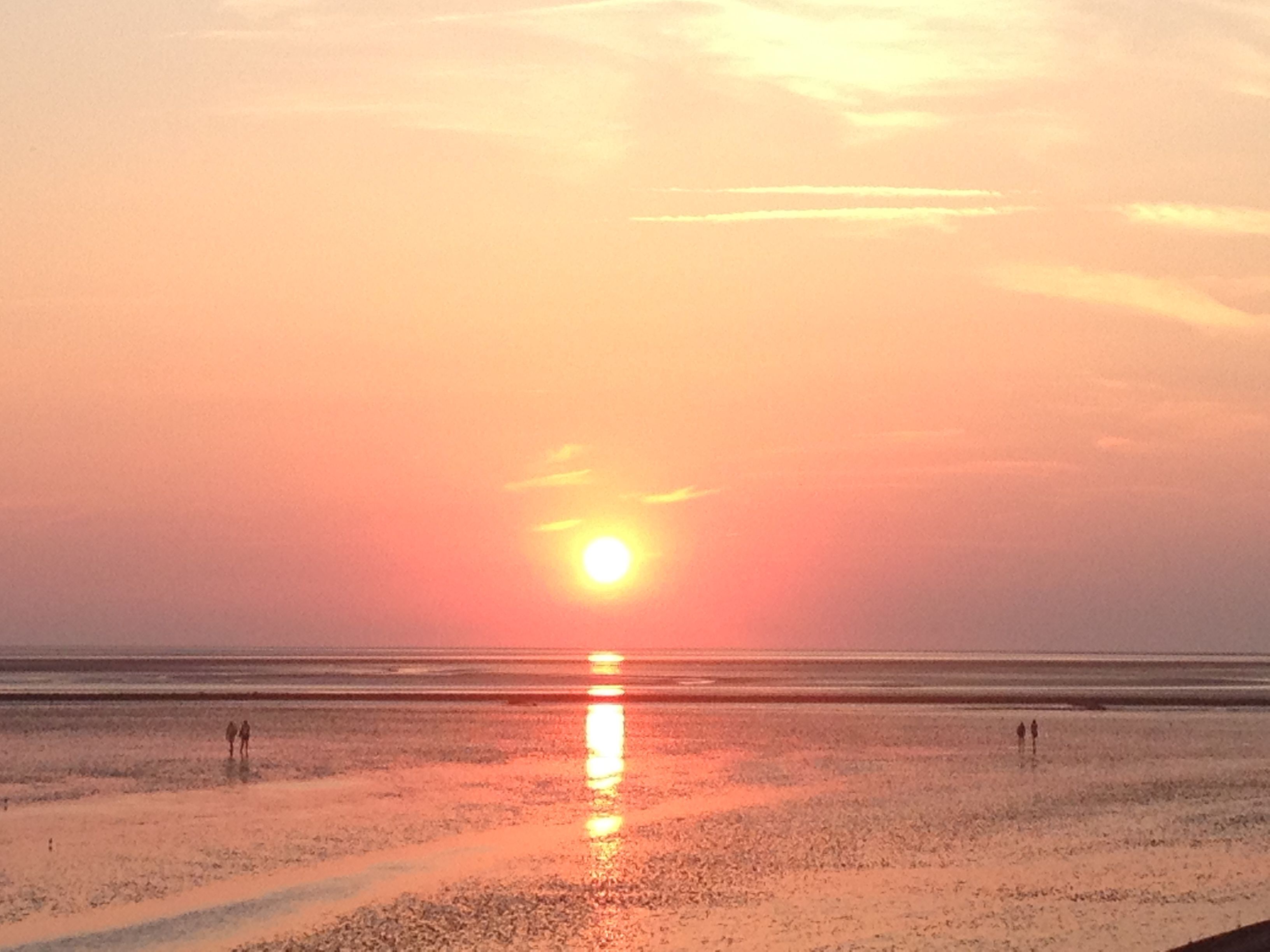 Ein Strand bei Sonnenuntergang mit ruhiger See und einigen Spaziergängern.