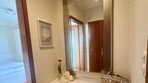 A bathroom with a white vanity, a mirror, a framed welcome sign, a red flower, and a woven basket. - A11 (BC.a5) - Stranddomicil Steiner (Büsum)