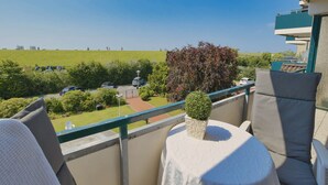 A balcony with a view of a parking area, a grassy field, and a building in the background. - A11 (BC.a5) - Stranddomicil Steiner (Büsum)