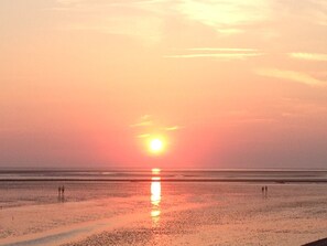 A beach at sunset with a calm sea and a few people walking. - A11 (BC.a5) - Stranddomicil Steiner (Büsum)