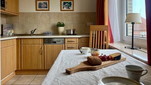 Een keuken met houten kasten, een vaatwasser, een eettafel met een witte tafelkleed en een raam met gordijnen.