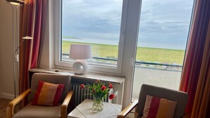 Una habitación con dos sillones, una mesita con un jarrón de flores, una lámpara y vistas al mar a través de amplios ventanales.