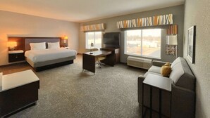 Habitación de hotel con cama, escritorio, silla, televisión y ventana grande.
