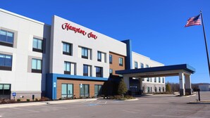 Un hotel Hampton Inn con fachada moderna, señalización clara y un estacionamiento.