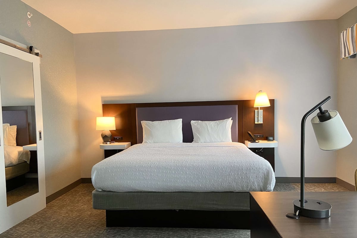 Hotellihuone, jossa on suuri sänky, kaksi yöpöytää valaisimineen, peili ja moderni lattiavalaisin.