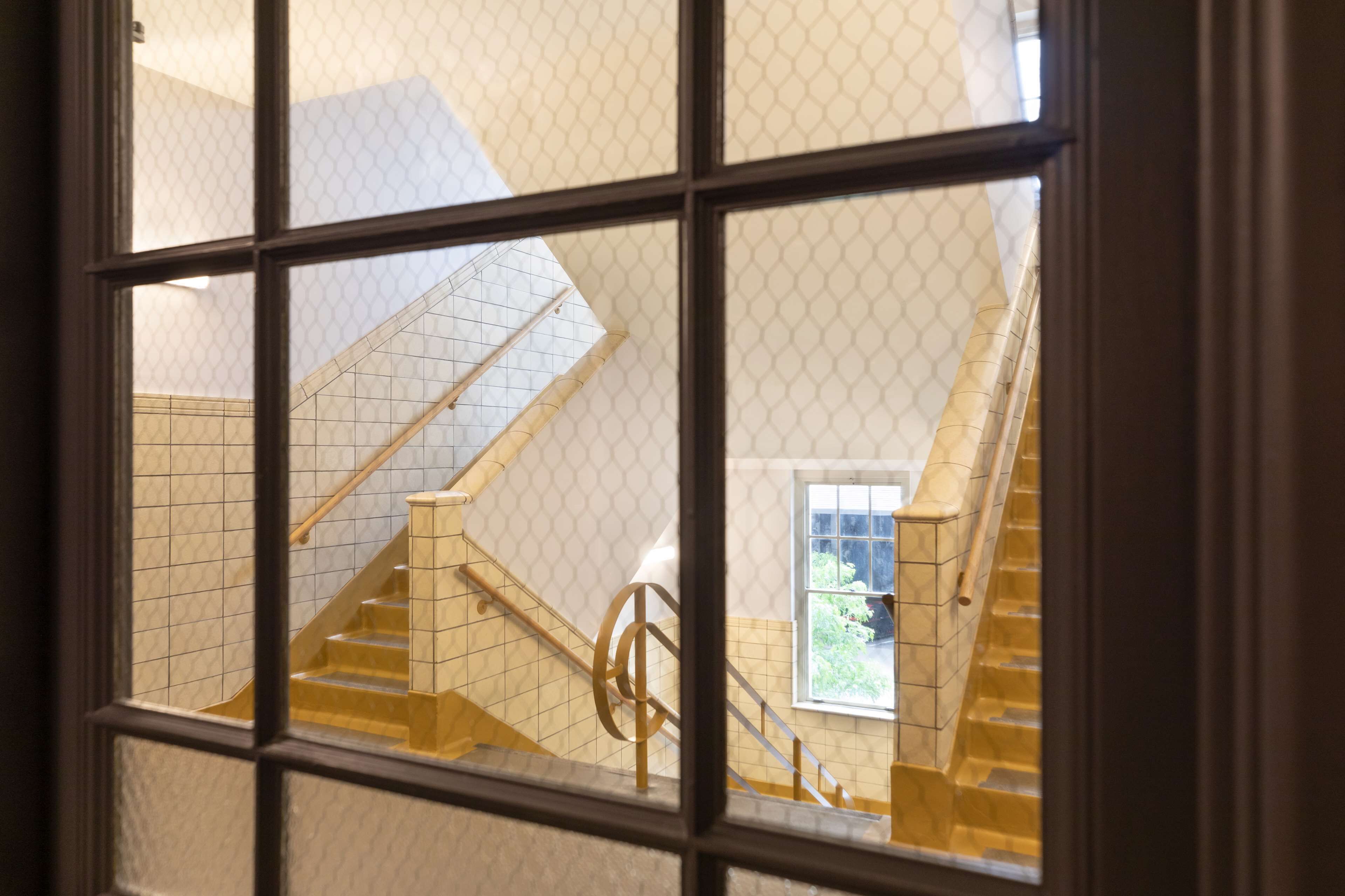 Blick durch ein Fenster auf eine Treppe mit Handlauf und einer Kachelwand.