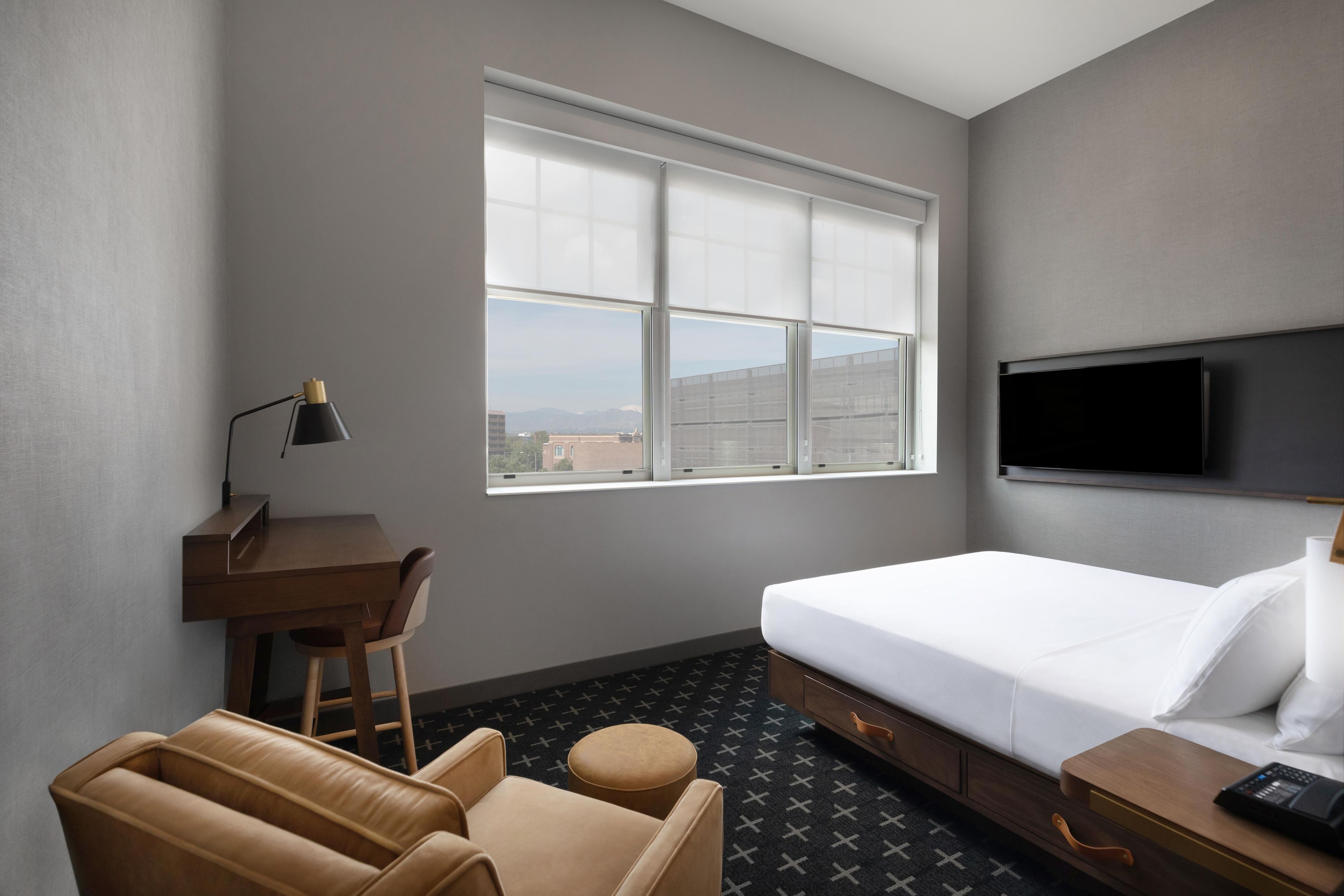Habitación de hotel con cama, escritorio, silla, sofá, televisor y ventana con vista a la ciudad.