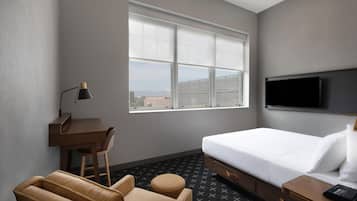 Habitación de hotel con cama, escritorio, silla, sofá, televisor y ventana con vista a la ciudad.