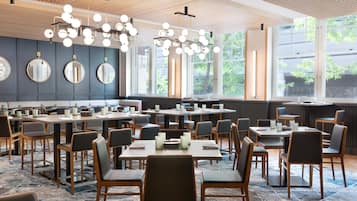 A modern restaurant with round tables and chairs, large windows, and a wooden ceiling.