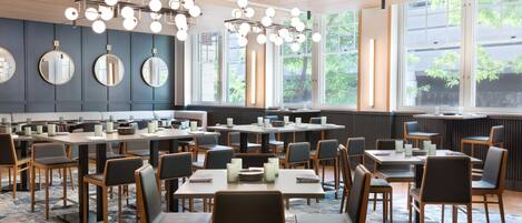 Un restaurante moderno con mesas y sillas redondas, ventanas amplias y techo de madera.