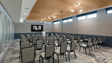 A conference room with rows of chairs, a wooden ceiling, and a large screen displaying 'THE SLATE TAPESTRY COLLECTION by Hilton'.