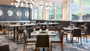 Un restaurant moderne avec des tables rondes, des chaises noires et un plafond orné de lambris en bois et de luminaires suspendus.