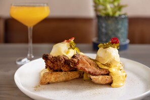 A plate with a breakfast dish, a glass of orange juice, and a potted plant in the background. - The Slate Denver, Tapestry Collection By Hilton (Denver)