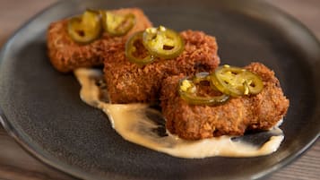 Trois morceaux de nourriture panés et frits, garnis de tranches de piment jalapeño, présentés sur une assiette sombre avec une sauce crémeuse.