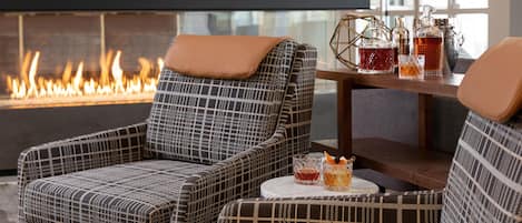 A cozy seating area with patterned chairs and a table with drinks, near a fireplace.