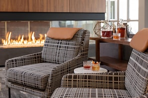 Un rincón acogedor con sillones estampados y una mesa con bebidas, cerca de una chimenea.