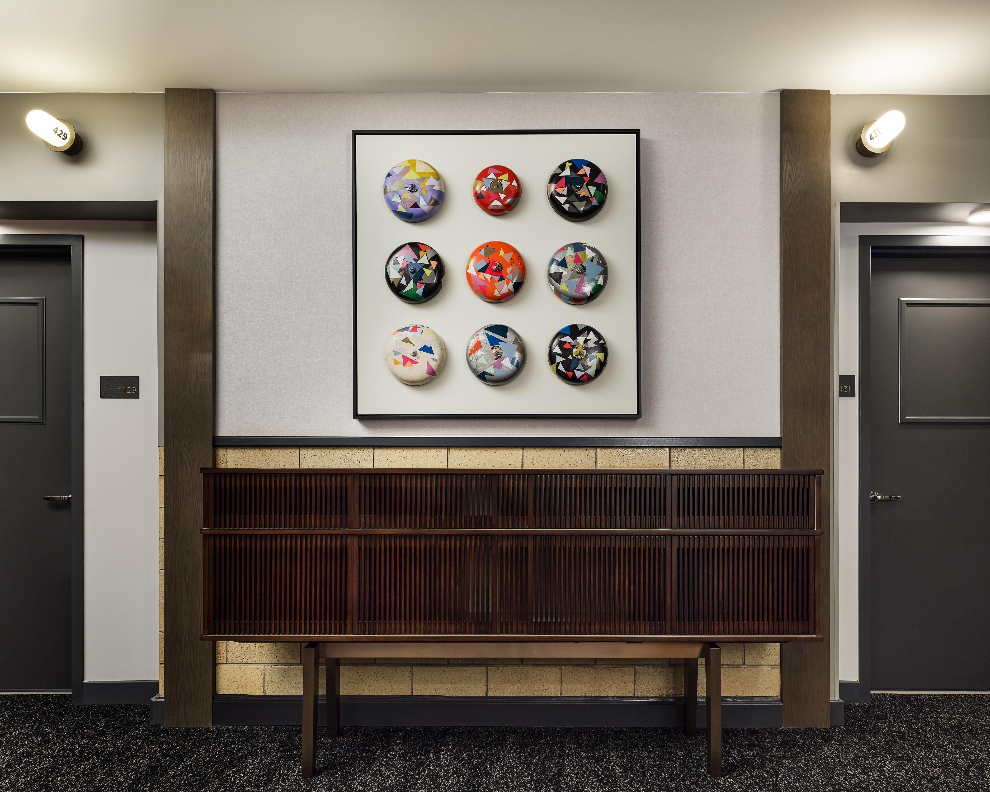 A lobby with a wall-mounted artwork of eight circular designs, a bench, and two doors with room numbers.