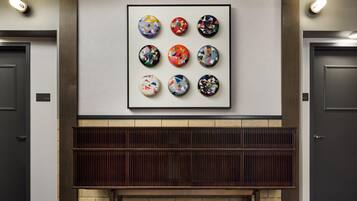 A lobby with a wall-mounted artwork of eight circular designs, a bench, and two doors with room numbers.