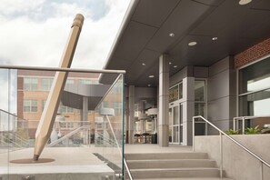 A modern building entrance with a glass railing, concrete steps, and a staircase leading to an upper level. - The Slate Denver, Tapestry Collection By Hilton (Denver)