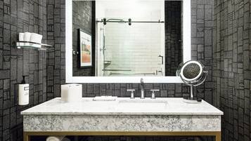 A bathroom with a marble sink, a large mirror, a towel dispenser, and a shower with a glass door.