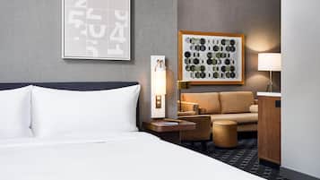 Une chambre d’hôtel avec un lit, une table de chevet, une lampe, un canapé et une œuvre d’art encadrée au mur.