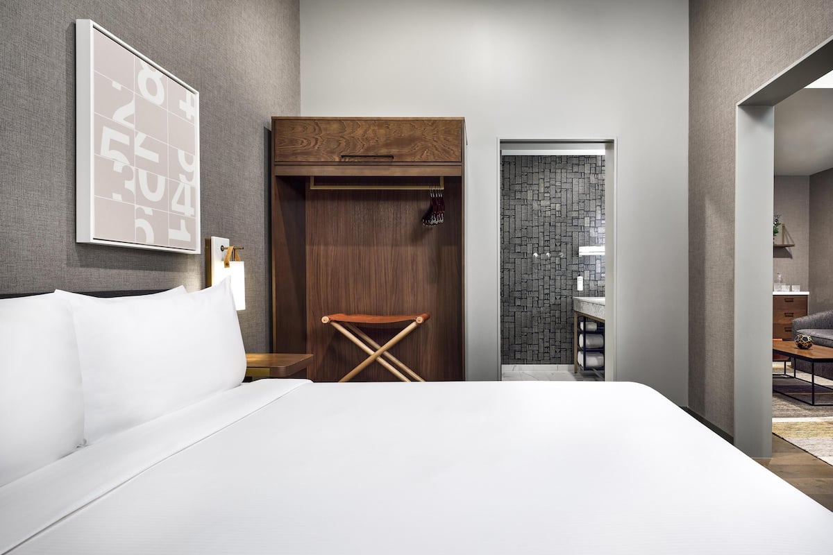 Un dormitorio moderno con una cama grande, un armario de madera, un taburete pequeño y un baño con pared de azulejos.
