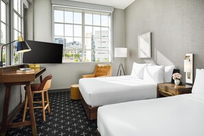 A hotel room with two beds, a desk, a chair, a TV, and a window with a city view. - The Slate Denver, Tapestry Collection By Hilton (Denver)