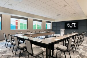 Un salón de conferencias con una larga mesa, sillas y una pantalla grande que muestra 'THE SLATE TAPESTRY COLLECTION by Hilton'.